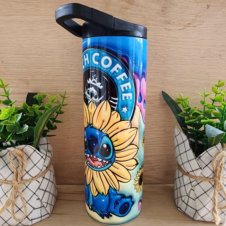 Puede incluir: Un vaso de acero inoxidable azul y amarillo con un dise&ntilde;o de personaje de dibujos animados. El personaje es Stitch de Lilo & Stitch, que lleva un girasol. El vaso tiene una tapa negra con asa y dice "Stitch Coffee" en el lateral.