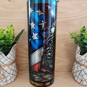 May include: A stainless steel tumbler with a blue, white, and red American flag design. A military boot is featured on the flag, with a film strip behind it.