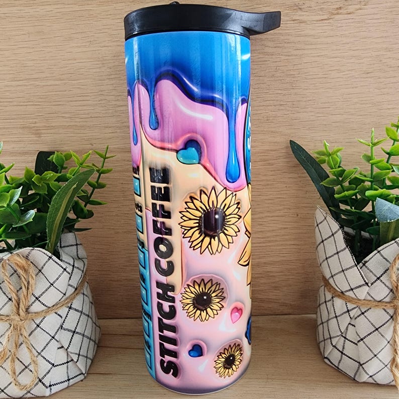 Puede incluir: Un vaso de acero inoxidable con un dise&ntilde;o de pintura rosa, azul y amarilla que gotea. El vaso tiene una tapa negra y un asa negra. El texto "Stitch Coffee" est&aacute; impreso en el lateral del vaso.