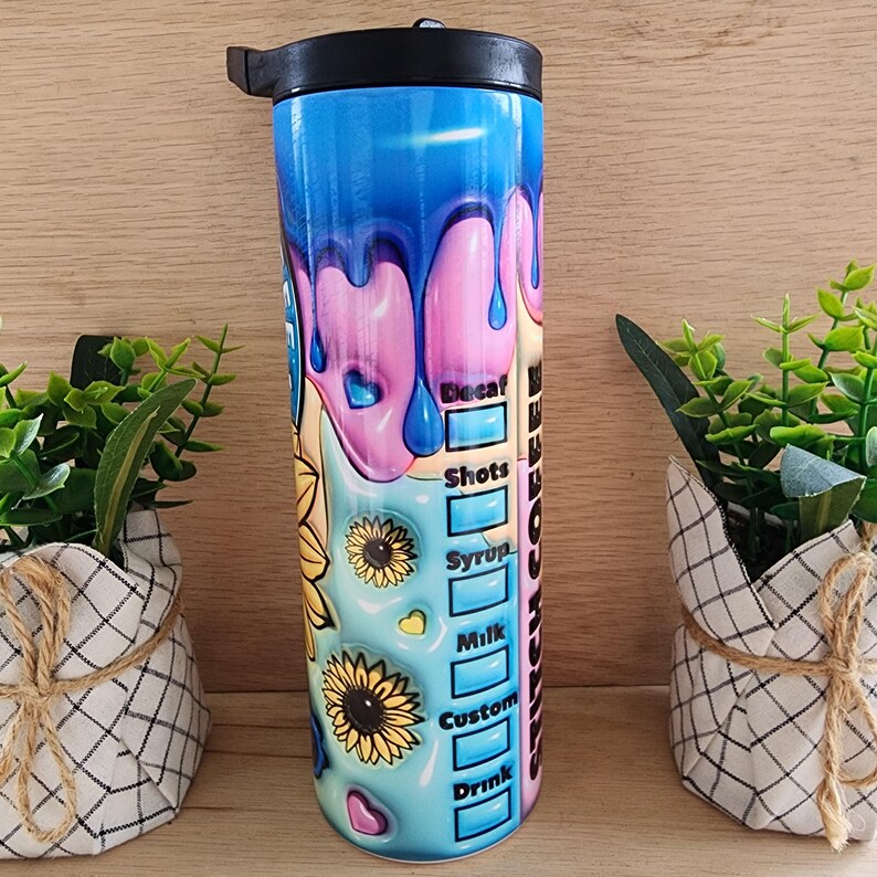 Puede incluir: Un vaso de acero inoxidable con un dise&ntilde;o colorido que presenta pintura goteando y girasoles. El vaso tiene una tapa y una pajita. El texto "Switch Coffee" est&aacute; impreso en el lateral del vaso.