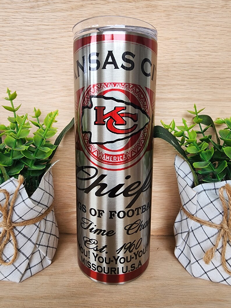 K&ouml;nnte beinhalten: Ein Edelstahlbecher mit einem roten und silbernen Design, das das Logo der Kansas City Chiefs, die Worte "Kansas City Chiefs", "Kings of Football", "Time Champs", "Est. 1960", "You! You-You-You!" und "Missouri U.S.A." zeigt.