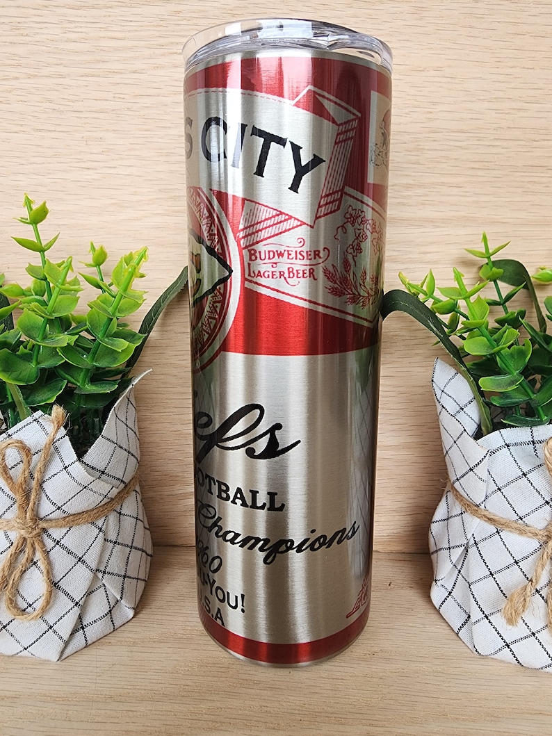 K&ouml;nnte beinhalten: Ein Edelstahlbecher mit einem rot-wei&szlig;en Budweiser-Etikett und dem aufgedruckten Text "City" und "Football Champions".