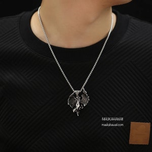 May include: A silver chain necklace with a pendant featuring a detailed design of a woman with wings. The pendant is made of metal and has a dark, aged finish. The necklace is worn by a person with a black shirt.