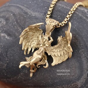 May include: Gold-toned pendant necklace featuring a detailed sculpture of a winged woman with outstretched wings. The pendant is attached to a gold chain.