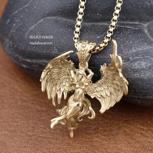 May include: Gold-toned pendant necklace featuring a detailed winged figure with a raised, textured design. The pendant is attached to a gold-toned chain.
