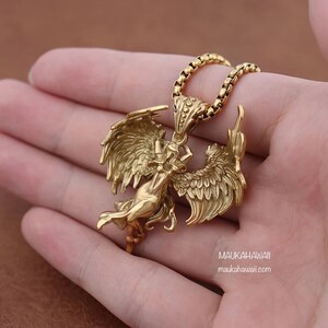 May include: Gold-toned necklace with a pendant featuring a detailed angel figure with wings spread wide. The pendant is attached to a gold chain.