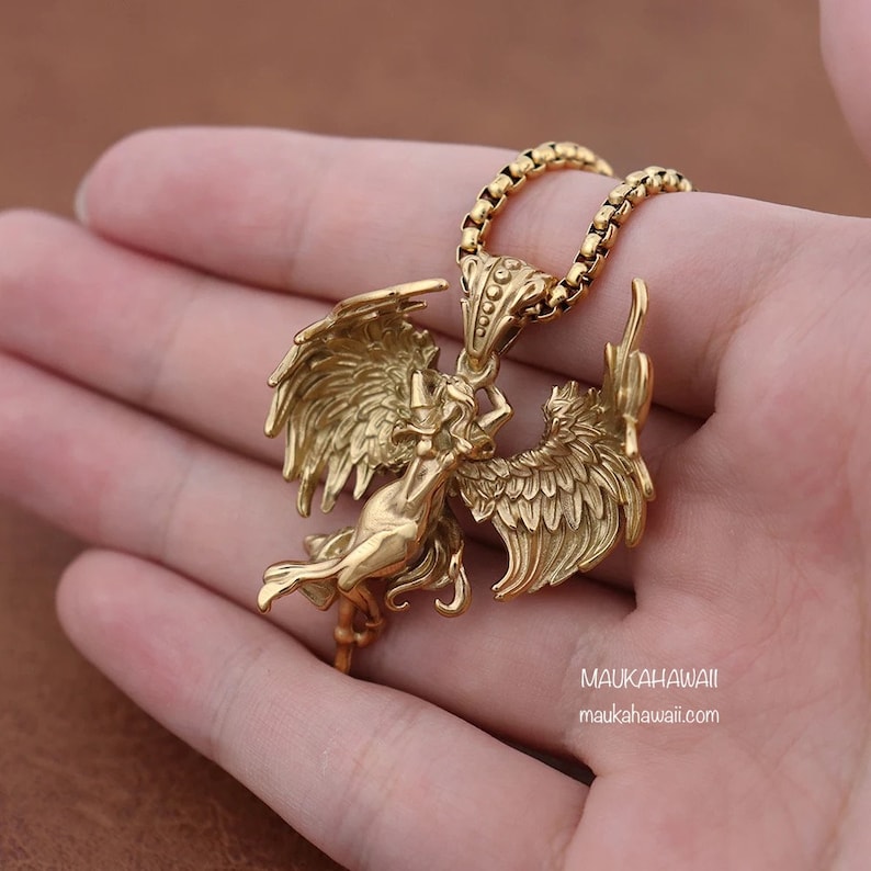 May include: Gold-toned necklace with a pendant featuring a detailed angel figure with wings spread wide. The pendant is attached to a gold chain.