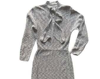 May include: A gray long-sleeved dress with a ruffled neckline and a tie at the neck.