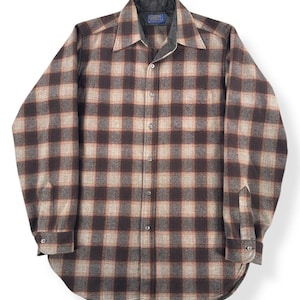 May include: A button-down, long-sleeve shirt in a brown, tan, and orange plaid pattern. The shirt has a pointed collar and buttoned cuffs. The interior collar is a dark gray quilted material. The shirt is made of a soft, woven fabric.