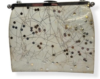 May include: A white clutch purse with a silver frame and a silver chain strap. The purse is covered in silver and gold sequins and has a white and silver abstract design.