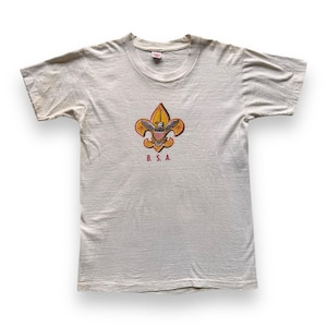 Könnte beinhalten: Cremefarbenes Kurzarm-T-Shirt mit einem farbenfrohen Fleur-de-Lis-Emblem, einem Adler und den Buchstaben "B.S.A." in Rot. Das Shirt hat einen Rundhalsausschnitt und einen leicht abgenutzten Look, was auf Vintage-Kleidung hindeutet.