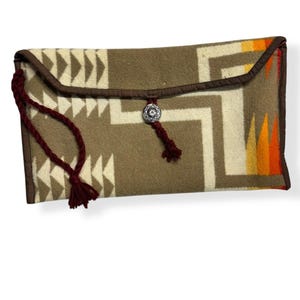 Puede incluir: Un bolso de mano marrón y blanco con estampado, con un borla roja y un cierre de botón plateado.