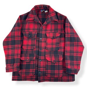 May include: A red and black plaid jacket with four front pockets and a button-up closure. The jacket has a collared neckline and long sleeves. The fabric appears to be a thick wool or wool blend. The jacket is a classic style.