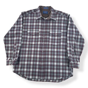 Puede incluir: Una camisa de franela abotonada de manga larga con un estampado de cuadros en burdeos, blanco y verde azulado. La camisa tiene dos bolsillos en el pecho y un cuello marrón. La etiqueta Pendleton es visible en el cuello.