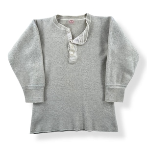 Pode incluir: Uma camisa Henley cinza de manga comprida com gola redonda e carcela de três botões. A camisa tem punhos canelados e um tecido texturizado. A camisa é de cor cinza lisa.