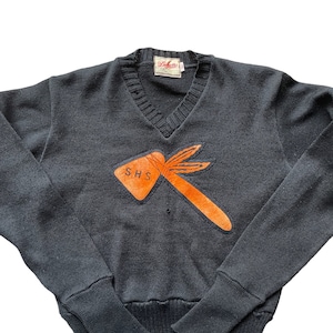 Puede incluir: Suéter negro de cuello en V con una aplicación naranja y marrón de un hacha con las letras "SHS" en ella. El suéter tiene una etiqueta que dice "Delmont".