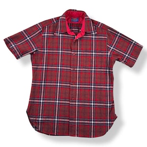 Peut inclure: Une chemise à manches courtes à carreaux rouges et marron. La chemise a un col rouge et une petite étiquette bleue. Le tissu semble être de poids moyen, adapté aux tenues décontractées. La chemise est boutonnée.
