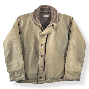 May include: A vintage olive drab jacket with a brown fur collar. The jacket has a button-up front, two front pockets, and a quilted lining. The jacket appears worn, with some stains and wear.