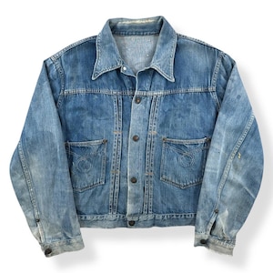 Puede incluir: Chaqueta vaquera vintage en un lavado azul claro. La chaqueta presenta un cuello clásico, cierre de botones, dos bolsillos en el pecho y puños abotonados. La mezclilla muestra signos de desgaste, lo que aumenta su atractivo vintage. Una prenda exterior clásica.