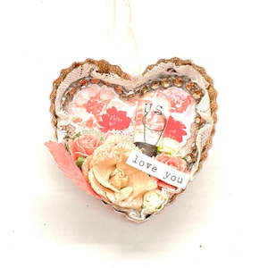 May include: A heart-shaped ornament featuring a floral pattern, a light bulb with the word "us" on it, and the words "love you" on a tag. The ornament is decorated with lace and glitter.
