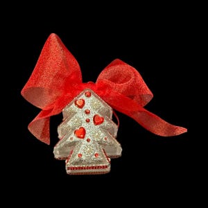 Puede incluir: Adorno decorativo de árbol de Navidad con un lazo rojo. El árbol plateado presenta detalles en forma de corazón rojo y adornos perlados. El adorno mide aproximadamente 7.6 cm de alto.
