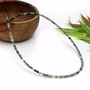 May include: A green agate beaded necklace with a light green and white colour variation. The necklace is made of small, round beads and is displayed on a white surface.