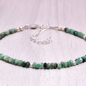Könnte beinhalten: Ein zartes Armband aus smaragdgrünen Edelsteinen mit einem silbernen Kettenverschluss. Das Armband besteht aus kleinen, facettierten Smaragdperlen.