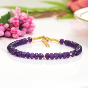 May include: A delicate amethyst gemstone bracelet with gold beads and a gold clasp. The bracelet is made with small, faceted amethyst beads and is perfect for everyday wear.