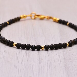 Peut inclure: Un bracelet en perles de pierres précieuses noires avec des accents dorés. Le bracelet est composé de perles noires facettées et de perles d'espacement dorées. Le bracelet est doté d'une fermeture à fermoir.