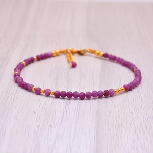 Könnte beinhalten: Ein zartes Armband aus rosafarbenen Edelsteinen mit goldenen Perlen und einem Schiebeverschluss.