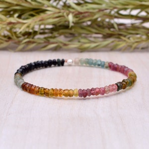 Könnte beinhalten: Ein mehrfarbiges Edelstein-Armband mit schwarzen, grünen, gelben, orangen, rosa und blauen Perlen. Das Armband besteht aus kleinen, facettierten Perlen und hat einen silbernen Verschluss.