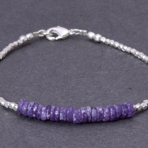 Puede incluir: Un brazalete de plata con una fila de cuentas de piedras preciosas moradas. El brazalete está hecho de pequeñas cuentas de plata facetadas.