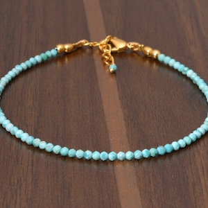 Może przedstawiać: Delikatny turkusowy naszyjnik z elementami w kolorze złotym. Naszyjnik wykonany jest z małych, fasetowanych koralików turkusowych i posiada zapięcie typu karabińczyk.