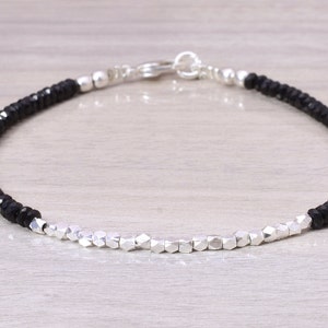 Könnte beinhalten: Ein schwarzes und silbernes Perlenarmband mit einem silbernen Verschluss. Das Armband besteht aus kleinen, facettierten schwarzen Perlen und größeren, silbernen Perlen.