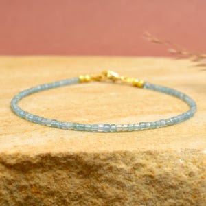 Könnte beinhalten: Ein zartes Armband mit kleinen, hellblauen Perlen. Das Armband wird mit einem goldfarbenen Verschluss und Akzenten verschlossen. Die Perlen sind gleichmäßig groß und bilden ein subtiles, elegantes Accessoire. Die Länge beträgt ca. 17-20 cm.