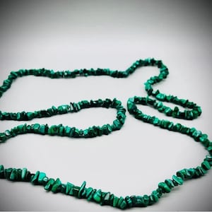 Op de afbeelding: Een lange ketting gemaakt van groene malachietstenen. De ketting is gemaakt van veel kleine, onregelmatige stenen die aan elkaar geregen zijn.