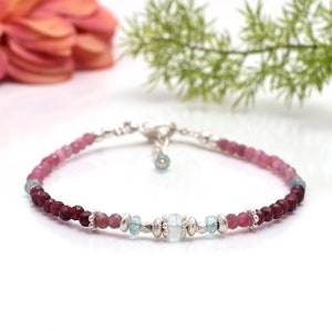 Może przedstawiać: Delikatny bransoletka z gradientem różowych i czerwonych kamieni szlachetnych, przeplatanych srebrnymi koralikami i jednym jasnoniebieskim kamieniem szlachetnym w środku.