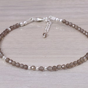 May include: A delicate anklet featuring small, faceted, smoky quartz beads strung together with silver-colored metal beads and a clasp. The adjustable chain allows for a customized fit. The anklet is designed to be worn around the ankle.