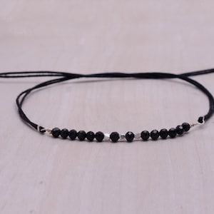 May include: A black beaded bracelet with silver accents on a black cord. The bracelet is adjustable with a sliding knot.