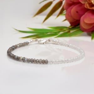 Puede incluir: Un brazalete de plata con un diseño de dos tonos. Una mitad del brazalete está hecha de cuentas de labradorita gris oscuro, mientras que la otra mitad está hecha de cuentas de cuarzo transparente.