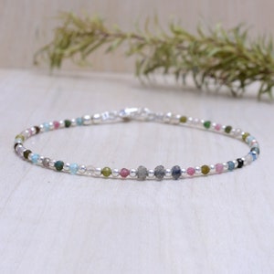 May include: A delicate silver bracelet featuring an assortment of colourful gemstones, including pink, blue, green, and grey. The bracelet is crafted with small, round beads and has a simple clasp.