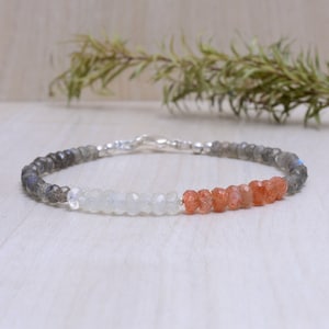Peut inclure: Un bracelet en argent avec des perles de pierres précieuses grises, blanches et orange. Le bracelet est fait de perles de labradorite, de pierre de lune et de pierre de soleil.
