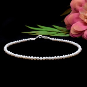 May include: A delicate white pearl necklace with a silver clasp. The necklace is made of small, round pearls and is perfect for everyday wear.