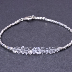 Può includere: Un braccialetto d'argento con una fila di cristalli trasparenti e sfaccettati e una chiusura in argento.