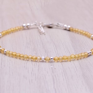 Może przedstawiać: Delikatny bransoletka wykonana z małych żółtych koralików z cytrynu i srebrnych koralików. Bransoletka ma srebrną klamrę.