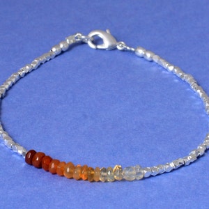 May include: A silver chain bracelet with a silver clasp and a row of orange, yellow, and white opal beads.