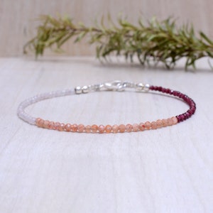 Könnte beinhalten: Ein zartes Armband mit einem Farbverlauf von hellrosa, orange und roten Perlen. Das Armband ist aus Sunstone-, Karneol- und Granatperlen gefertigt.