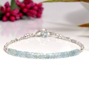 May include: A delicate silver bracelet with a row of light blue aquamarine beads. The bracelet has a simple clasp closure.