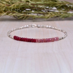 Könnte beinhalten: Ein zartes Silberarmband mit einer abgestuften Reihe von roten und rosafarbenen Edelsteinperlen.