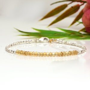May include: A delicate bracelet featuring a row of small, light yellow gemstones set in silver.